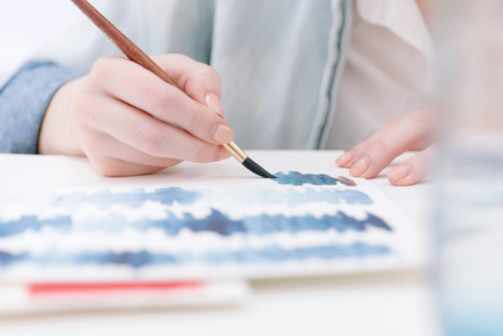 Person painting with watercolor brushes